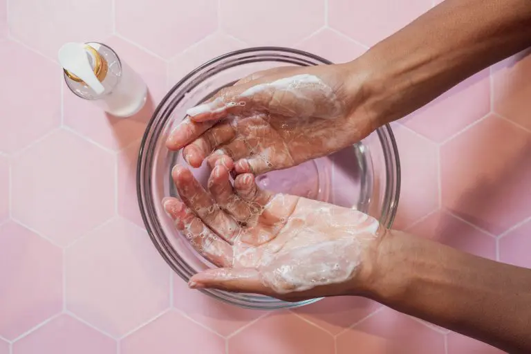 Hands washing with soap in bowl on pink tiles.