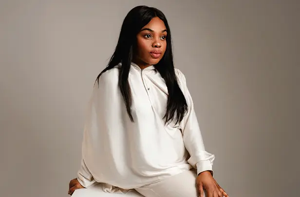 Woman in white outfit sitting against gray background.