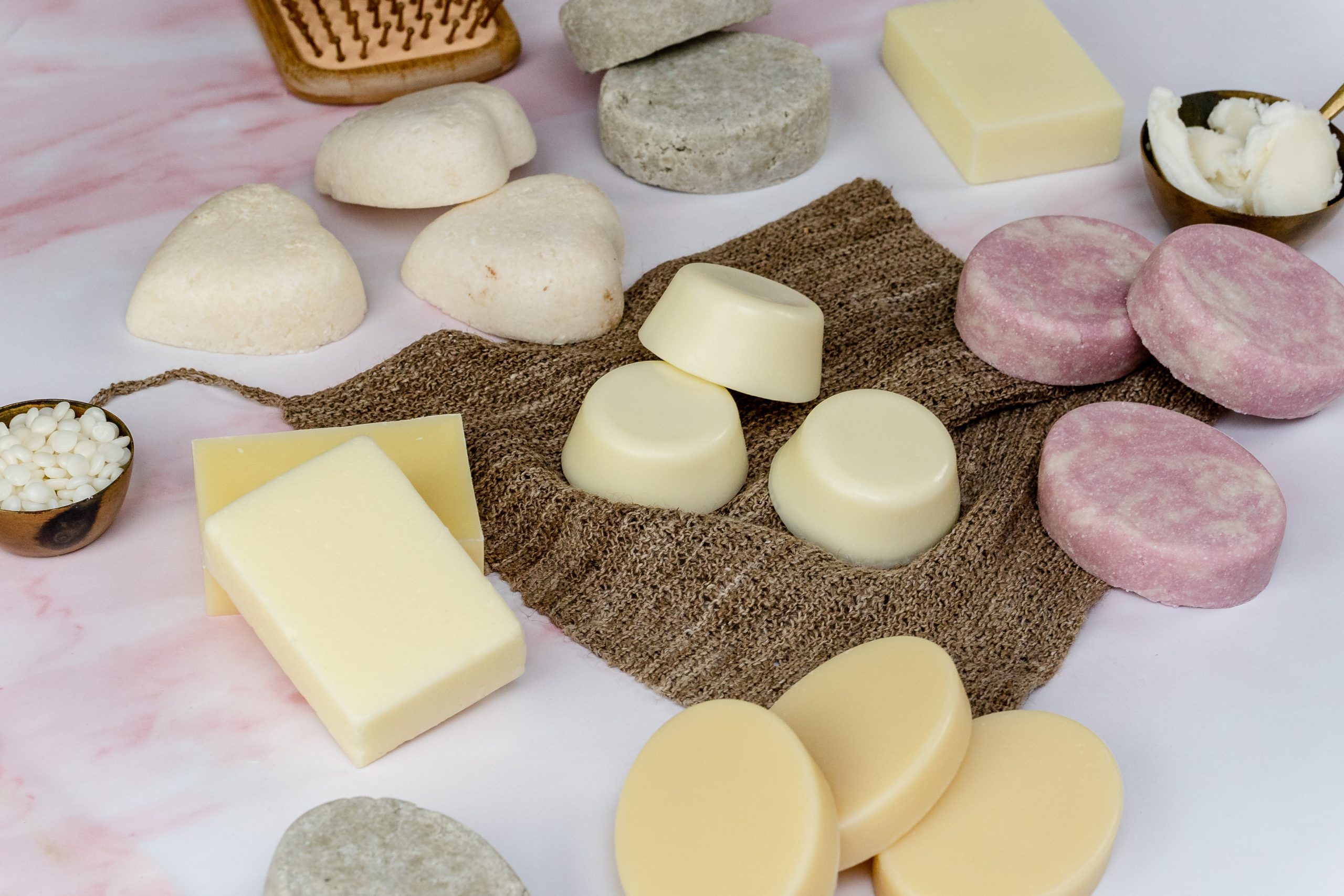Various handmade solid shampoo and conditioner bars on a pink background
